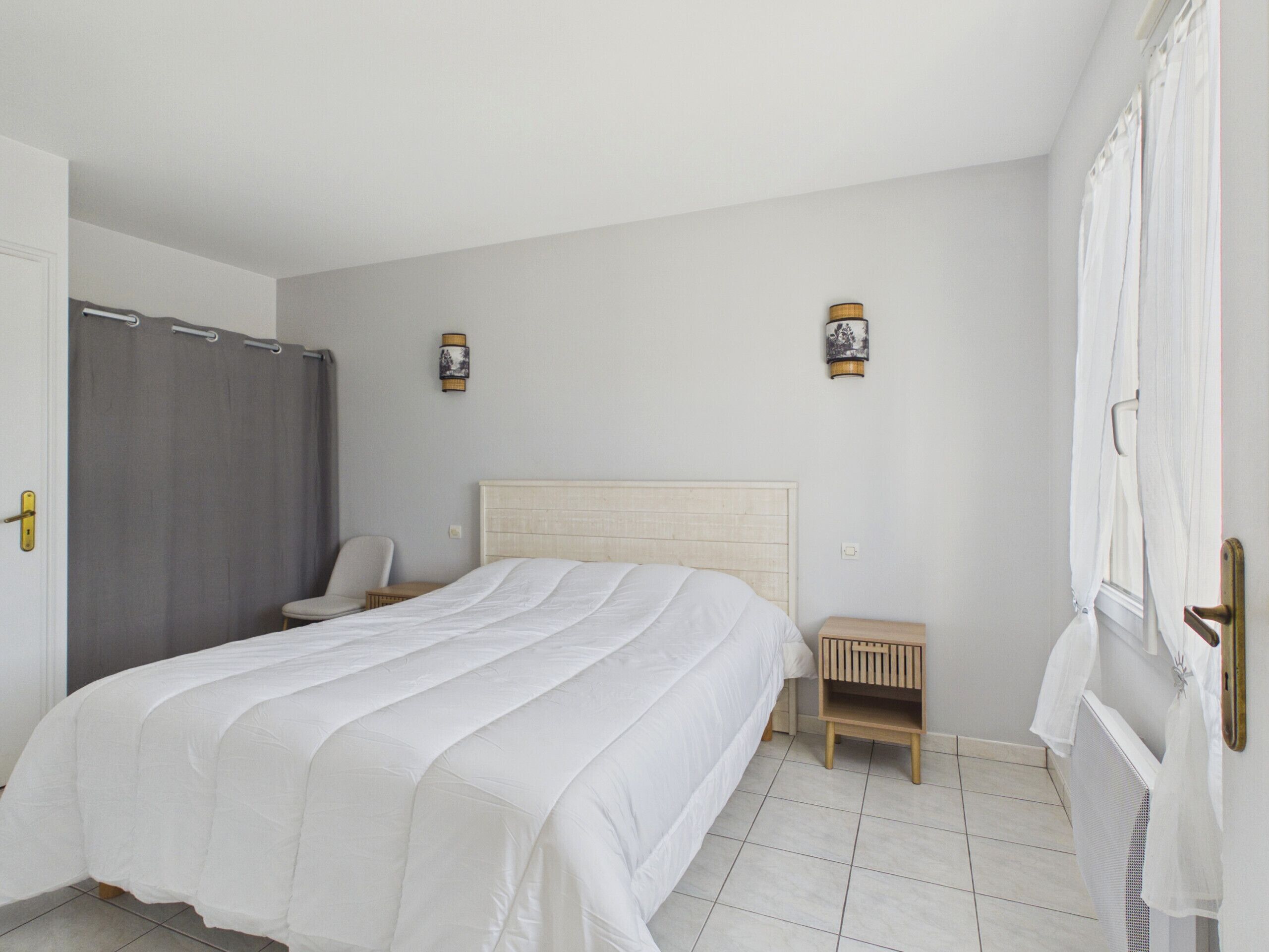 A bedroom with a bed, a chair, a nightstand, and a wall-mounted lamp.