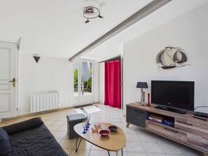 A modern living room with a sofa, a coffee table, a flat-screen TV, and a dining area with chairs and a table. - House and garden for 3 near the beach (La Plaine-sur-Mer)