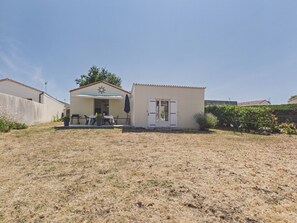 Ein kleines Gebäude mit überdachter Terrasse, einer Tür und einem kleinen Garten.