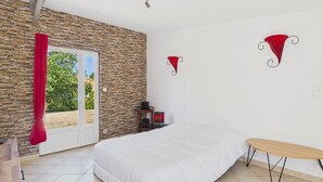 Ein Schlafzimmer mit einem Bett, einer Bank, einer Steinwand, einer Tür und einem kleinen Tisch mit einem roten Gegenstand darauf.