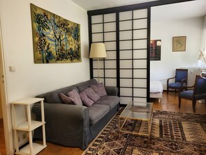 Uma sala de estar com sofá, mesa de centro, luminária, poltrona e tapete estampado.
