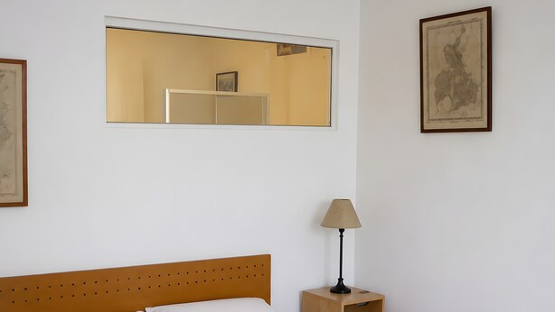 A neatly made bed with a wooden headboard, a bedside table with a lamp, and two framed pictures on the wall. - Apartment 'Studio Cannes Gallia' (Cannes)