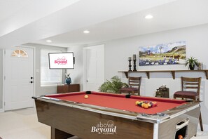 A pool table in a room with a door, a window with blinds, a painting on the wall, and a sign with 'above Beyond Hosting' text. - Lake Views | Treehouse, Fire Pit + Game Room | Family Fall Vacation! (Lago Vista)