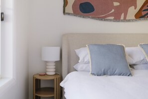 A bedroom with a bed, pillows, a bedside table, a lamp, and a wall art piece.