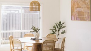 A dining area with a round wooden table, six wicker chairs, a hanging wicker pendant light, and a potted plant.