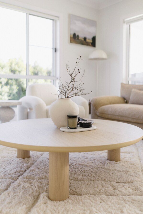 A round wooden table with a white vase and a small container on it, surrounded by a fluffy white rug.