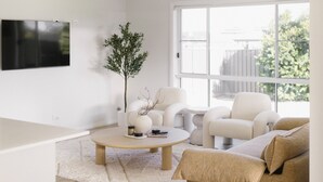 A modern living room with a flat-screen TV mounted on the wall, a round coffee table, a beige sofa, and a white armchair.