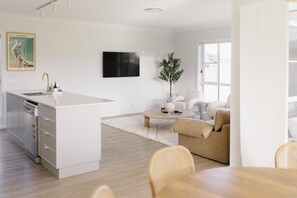 Moderni keittiö, jossa on keskeinen saareke, ruokailutila pyöreän pöydän kera sekä olohuone, jossa on sohva ja sohvapöytä.
