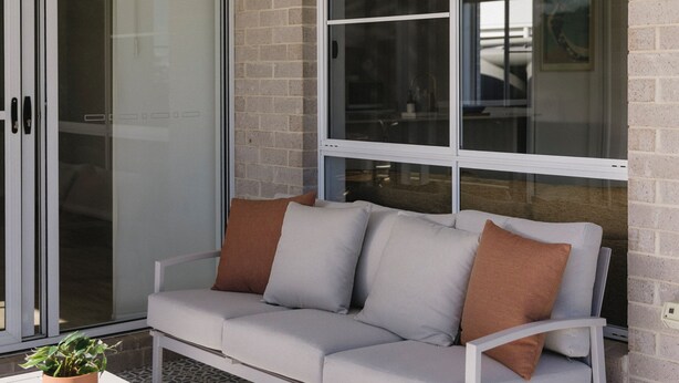 A modern outdoor seating area with a sofa and a table, a sliding glass door, and a brick wall.