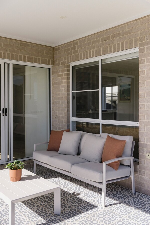 A modern outdoor seating area with a sofa and a table, a sliding glass door, and a brick wall.