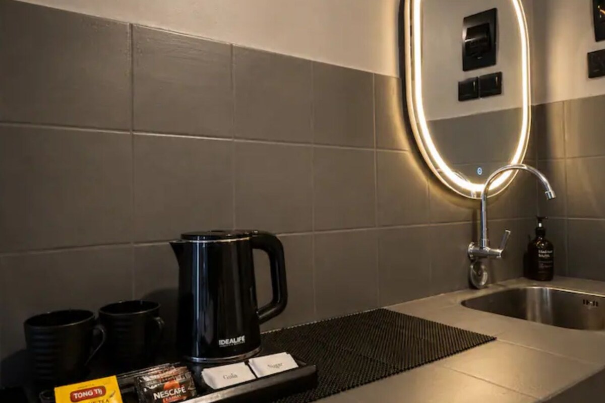 A modern bathroom with a coffee station, a mirror with a light, and a sink.