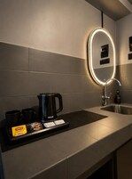 Un baño moderno con estación de café, un espejo con luz y un lavamanos.