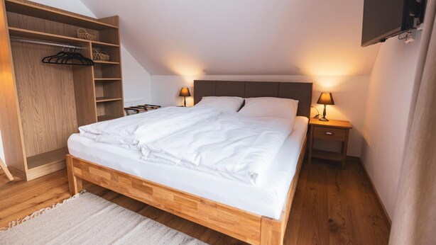 Une chambre à coucher avec un lit en bois, des tables de chevet, une armoire et un téléviseur fixé au mur.