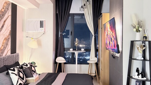 Quarto moderno com cama, mesas de cabeceira, televisão e vista da cidade à noite.