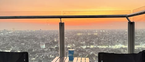 Un balcón con mesa y sillas, con vista a un paisaje urbano al atardecer.