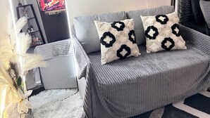 Uma sala de estar moderna com um sofá cinza, almofadas decorativas, um tapete branco felpudo e obras de arte nas paredes.