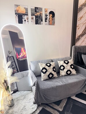 A modern living room with a grey sofa, decorative pillows, a fluffy white rug, and wall art. - Cozy Condo in Quezon City with City lights, Roof Deck & Netflix - Near SM North (Quezon City)