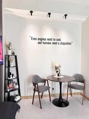 A modern room with a round table, two chairs, a bookshelf, and a decorative quote on the wall. - Cozy Condo in Quezon City with City lights, Roof Deck & Netflix - Near SM North (Quezon City)