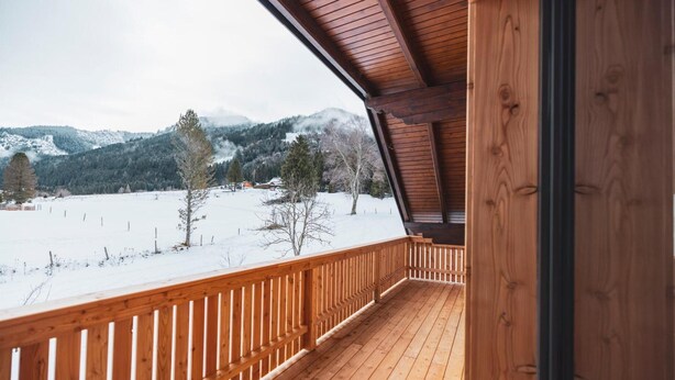 Ein Holzbalkon mit Blick auf eine verschneite Landschaft und Berge.
