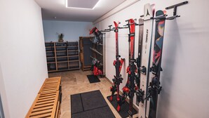 Ein Skiraum mit Skiern und Skistöcken auf Ablagen, eine hölzerne Sitzbank und ein kleiner Topf mit Pflanze auf einem Regal.