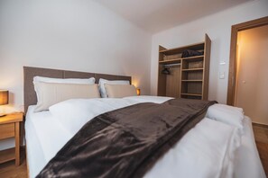 A neatly made bed with a headboard, a bedside table with a lamp, and a wooden wardrobe with shelves.