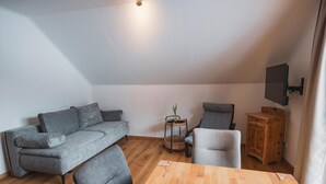 Ein modernes Wohnzimmer mit einem grauen Sofa, einem Holzesstisch und einem an der Wand montierten Fernseher.