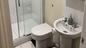 Et moderne badeværelse med en glasbrusekabine, toilet, vask med spejl og et håndklædestativ.