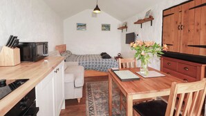 Una habitación acogedora con una cama, una mesa de comedor con sillas, una pequeña cocina y un armario de madera.