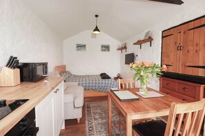 Ein gemütliches Zimmer mit einem Bett, einem Esstisch mit Stühlen, einer kleinen Küchenzeile und einem Holzschrank.