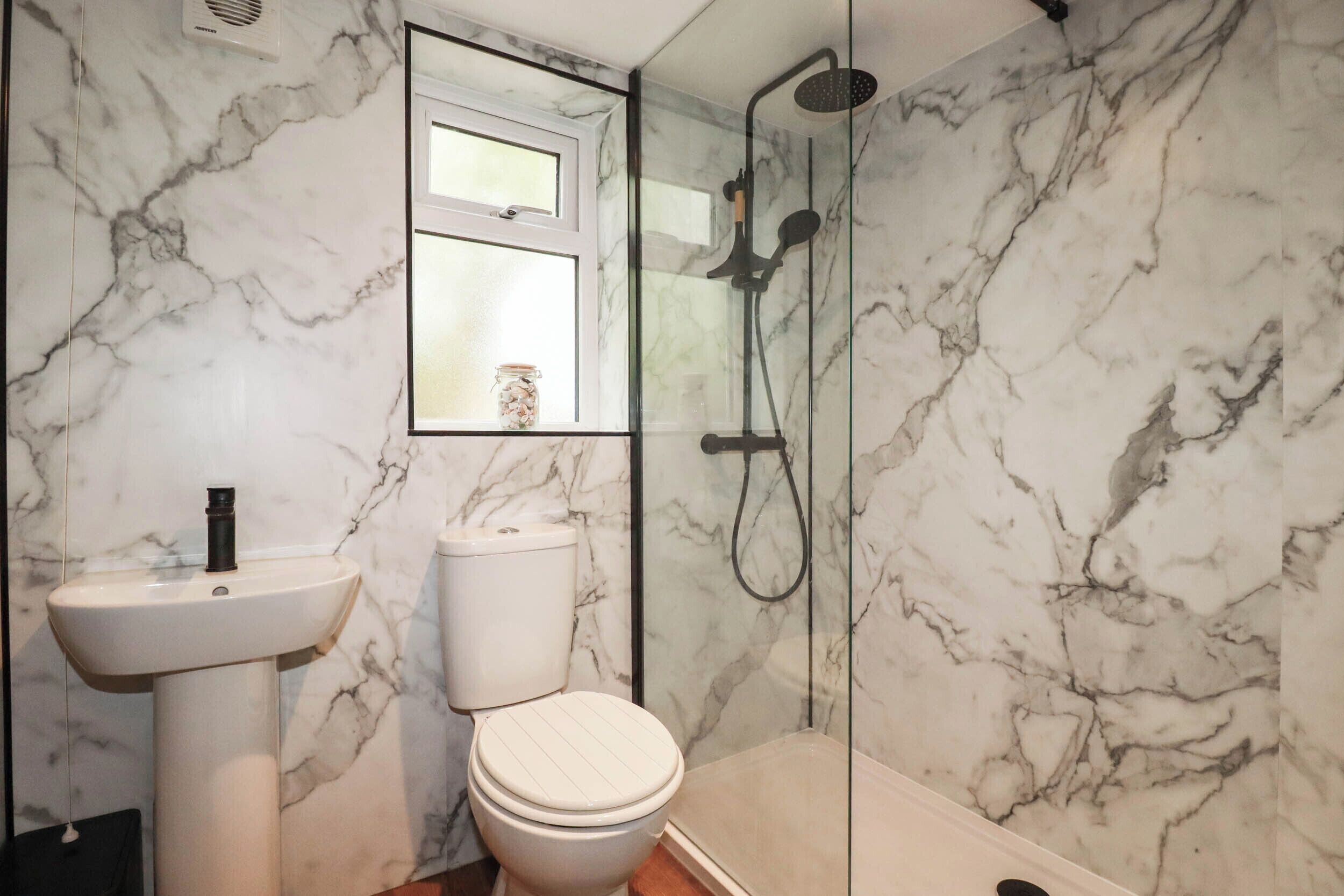 A bathroom with a marble wall, a toilet, a sink, and a shower enclosure.