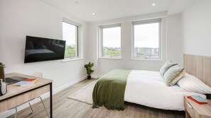 A modern bedroom with a bed, a desk with a laptop, a TV, and large windows. - Student Only The Sailworks (Lancaster)