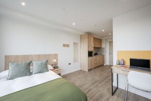 Ein Hotelzimmer mit Bett, Schreibtisch mit Laptop, einer Küchenzeile und einem Badezimmer.
