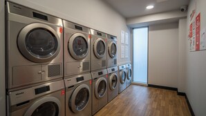 A laundry facility with multiple washing machines and dryers, a wooden floor, and a door leading to another room. - Student Only The Sailworks (Lancaster)