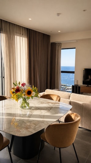A modern dining area with a marble table, a vase of flowers, and a view of the ocean through large windows. - Luxury 26th Floor Apartment with Panoramic Sea Views Mercury Towers St Julian (St. Julian's)
