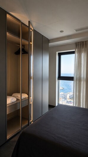 A hotel room with a bed, a wardrobe with a mirror, and a window with a city view. - Luxury 26th Floor Apartment with Panoramic Sea Views Mercury Towers St Julian (St. Julian's)