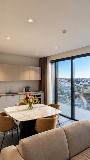 Ein modernes Wohnzimmer mit einem Marmortisch, einem beigefarbenen Sofa und Blick auf die Stadt durch große Fenster.