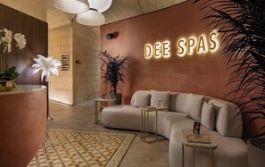 A modern interior with a curved sofa, a potted plant, and a wall-mounted sign reading 'DEE SPAS'. - Luxury 26th Floor Apartment with Panoramic Sea Views Mercury Towers St Julian (St. Julian's)