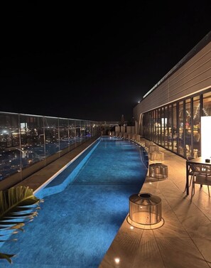 A rooftop pool with a glass balustrade, a dining area with tables and chairs, and a cityscape view at night. - Luxury 26th Floor Apartment with Panoramic Sea Views Mercury Towers St Julian (St. Julian's)