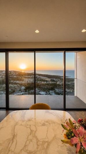 A modern interior with a large window overlooking a coastal landscape during sunset. - Luxury 26th Floor Apartment with Panoramic Sea Views Mercury Towers St Julian (St. Julian's)