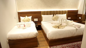 Habitación de hotel con dos camas, cabecero de madera, ropa de cama blanca y una alfombra roja con estampado.