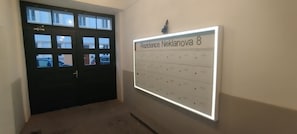 Un pasillo con una puerta negra y un cartel iluminado fijado a la pared.