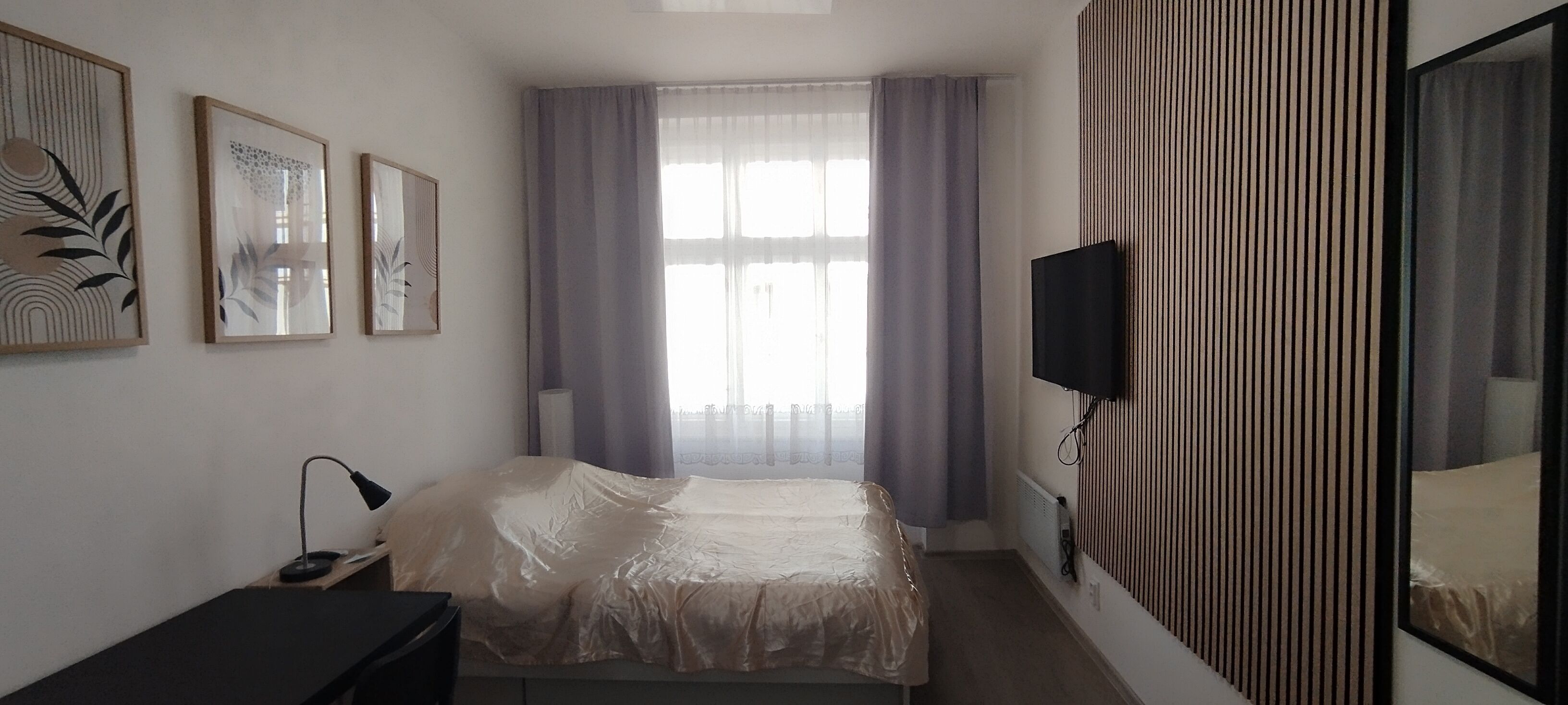Une chambre à coucher avec un lit, un bureau, une chaise, un téléviseur et une fenêtre avec des rideaux.