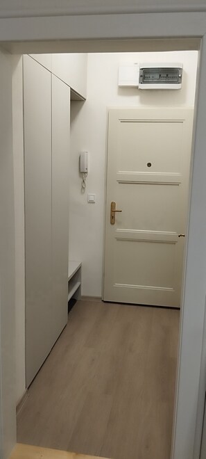 Un pasillo estrecho con una puerta blanca, un estante pequeño y un equipo de aire acondicionado fijado a la pared.