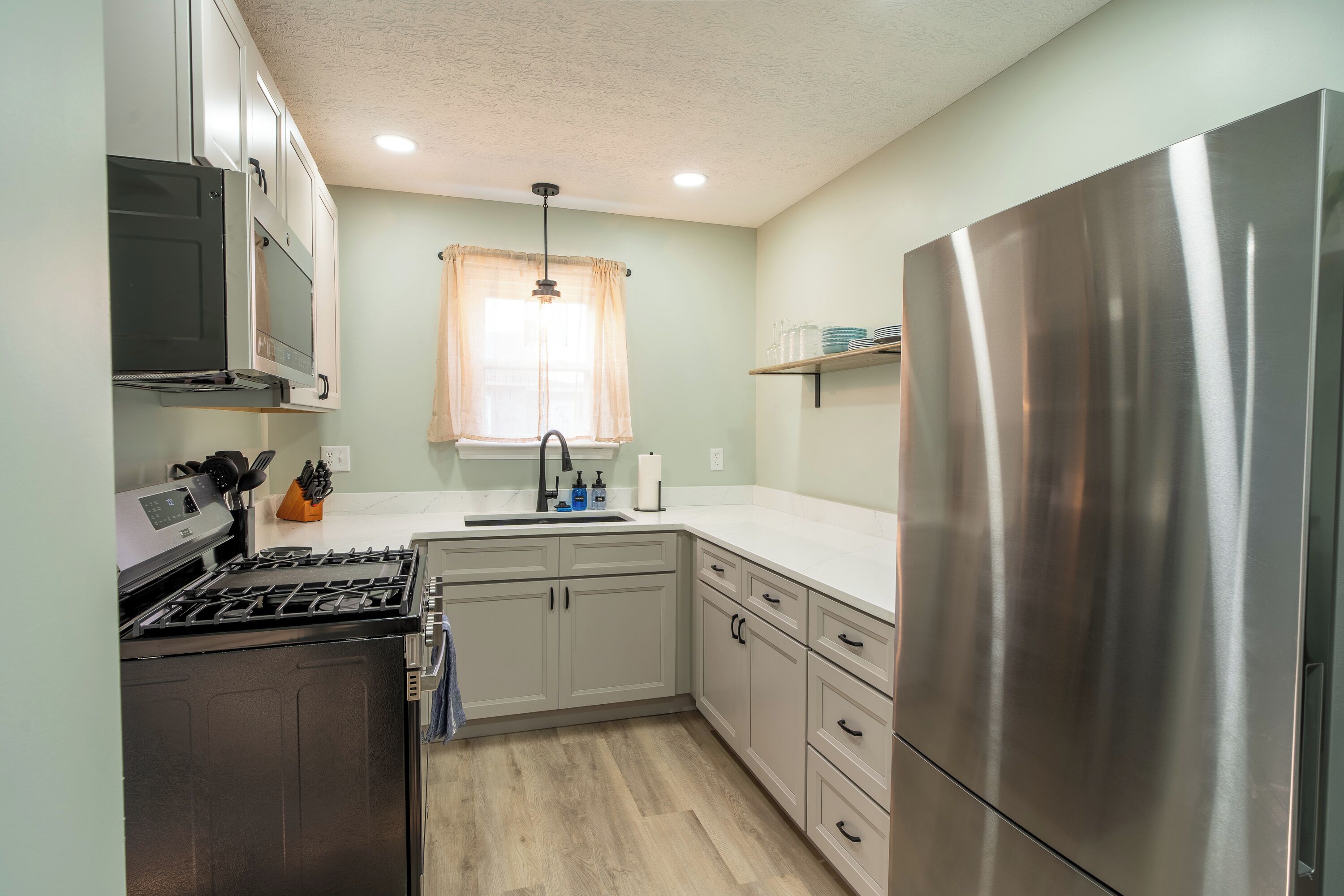 A compact kitchen with a stainless steel refrigerator, a built-in oven, and a microwave.