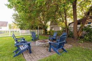 Un patio con sillas Adirondack, un hogar de piedra y una cerca de piquetes blancos.