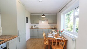 Una cocina con una mesa de comedor preparada para cuatro personas, sillas de madera y una ventana con vistas a la vegetación.