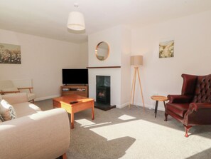 A living room with a sofa, a coffee table, a TV, a fireplace, a lamp, and a chair. - Wilpol (Llanerchymedd)