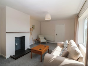 A living room with a fireplace, a sofa, a coffee table, and a lamp. - Wilpol (Llanerchymedd)