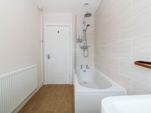 A bathroom with a white bathtub, a showerhead, and a white door. - Wilpol (Llanerchymedd)