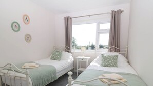 Un dormitorio con dos camas individuales, una mesita de noche pequeña, una ventana con cortinas y adornos en la pared.